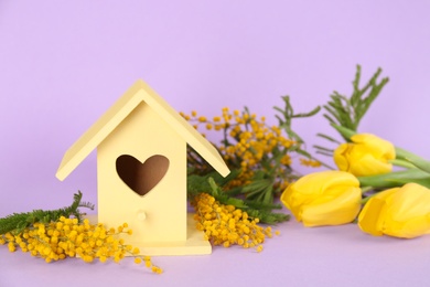 Photo of Stylish bird house and fresh flowers on violet background