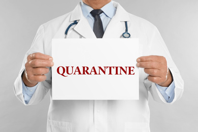 Image of Doctor holding sign with text QUARANTINE on light grey background, closeup. Stay at home during coronavirus outbreak