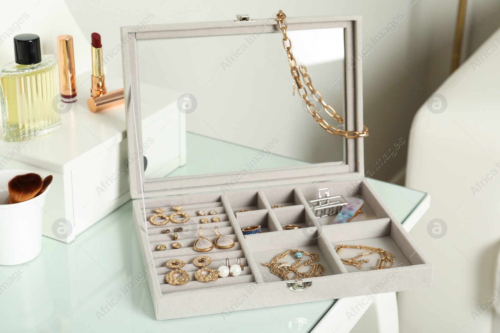 Photo of Elegant jewelry box with beautiful bijouterie, cosmetics and perfume on dressing table in room