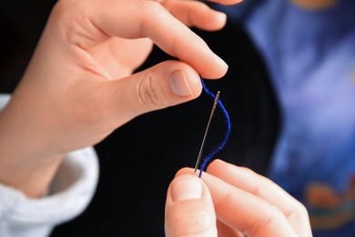 Woman threading sewing needle on blurred background, closeup