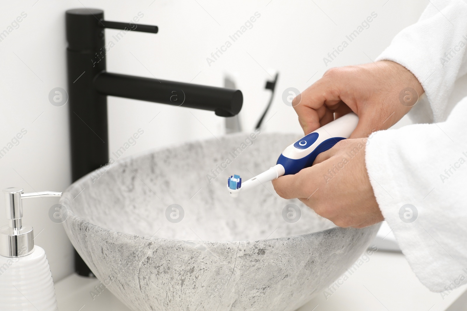 Photo of Man holding electric toothbrush above sink in bathroom, closeup