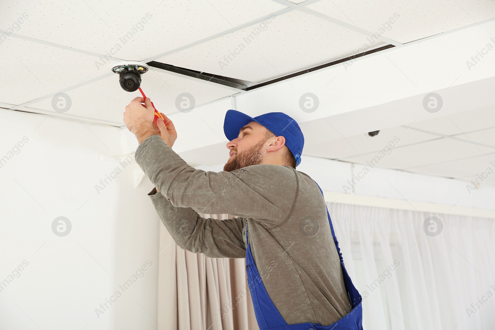 Photo of Electrician with screwdriver repairing CCTV camera indoors