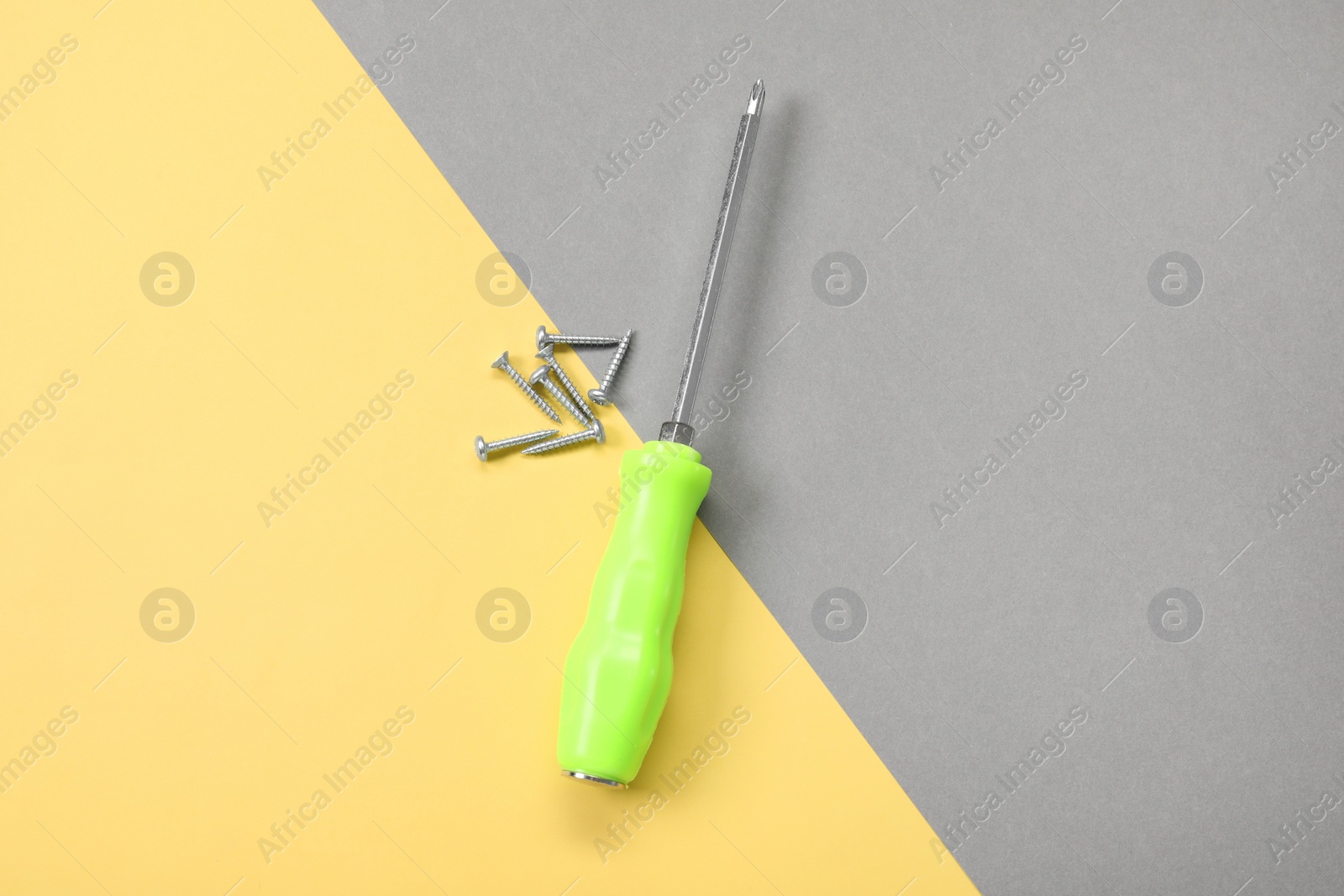 Photo of Screwdriver with green handle and screws on color background, flat lay