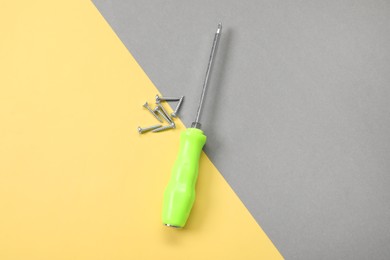 Photo of Screwdriver with green handle and screws on color background, flat lay