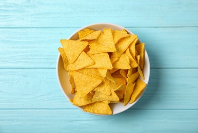 Photo of Tasty mexican nachos chips in bowl on blue wooden table, top view