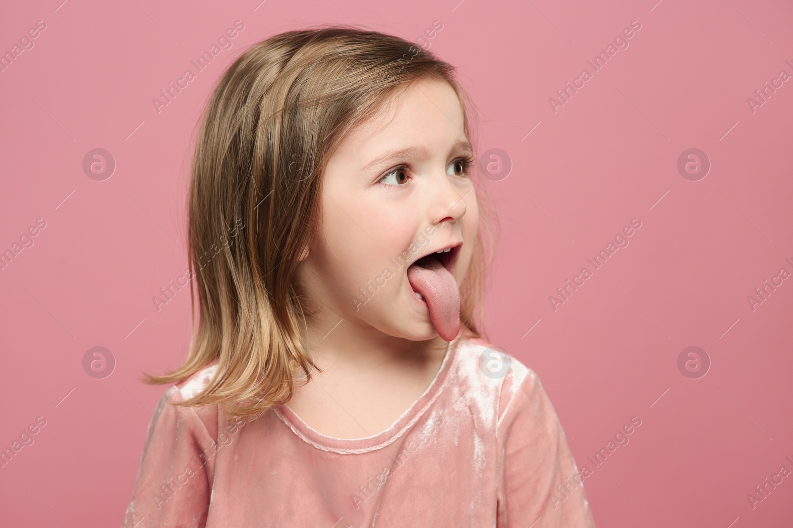 Photo of Funny little girl showing her tongue on pink background