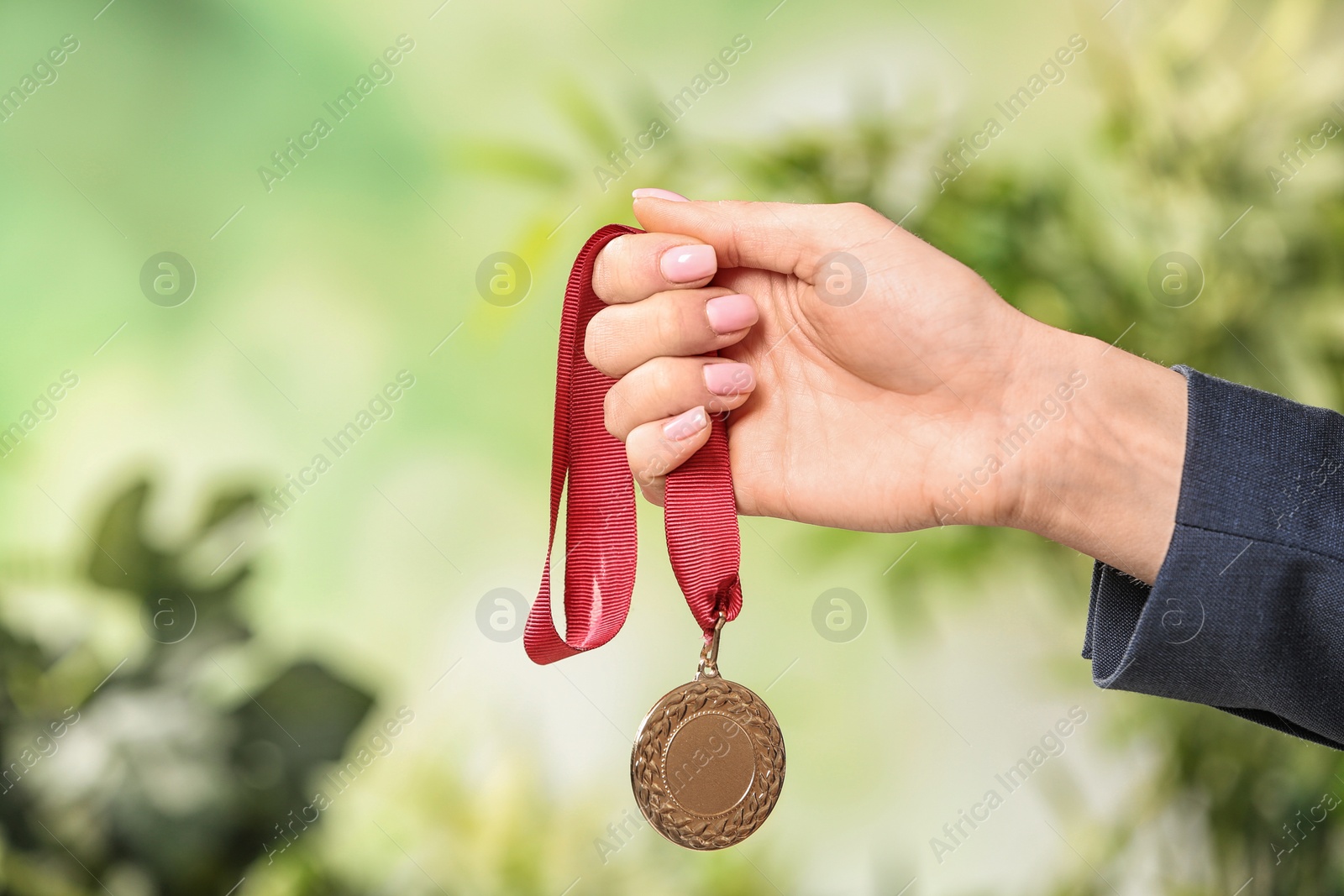 Photo of Woman holding gold medal on blurred background, closeup. Space for text