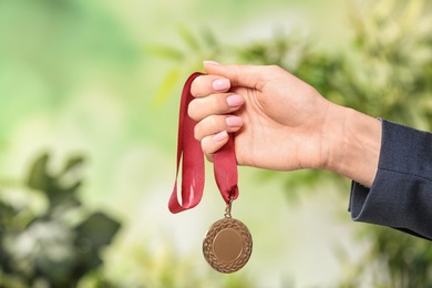 Photo of Woman holding gold medal on blurred background, closeup. Space for text