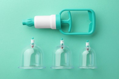 Photo of Plastic cups and hand pump on turquoise background, flat lay. Cupping therapy