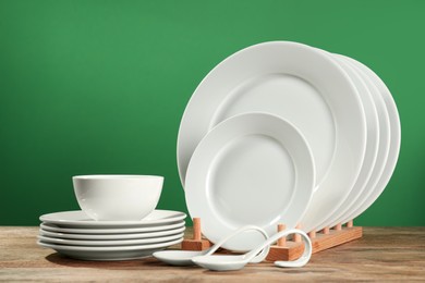 Photo of Set of clean dishware on wooden table against green background
