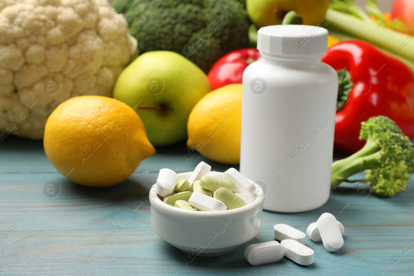 Photo of Dietary supplements. Blank white bottle and bowl with different pills near food products on light blue wooden table, closeup