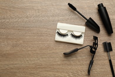 Photo of False eyelashes, curler, brush and mascara on wooden table, flat lay. Space for text