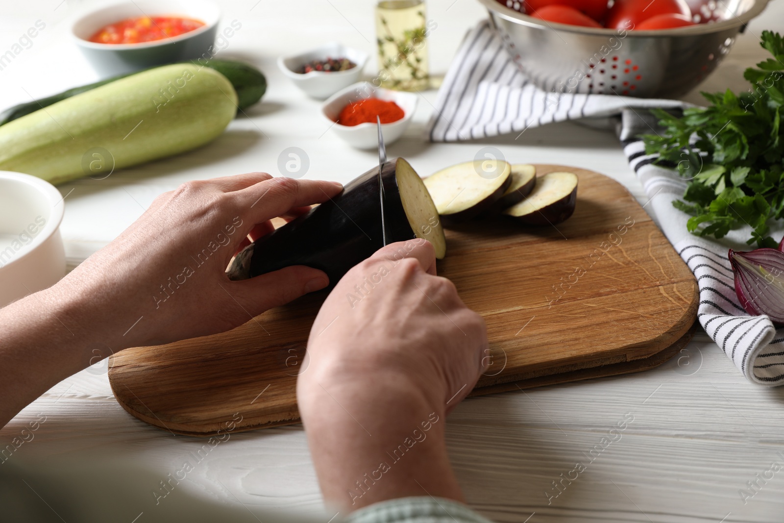 Photo of Cooking delicious ratatouille. Woman cutting fresh eggplant at white wooden table, closeup