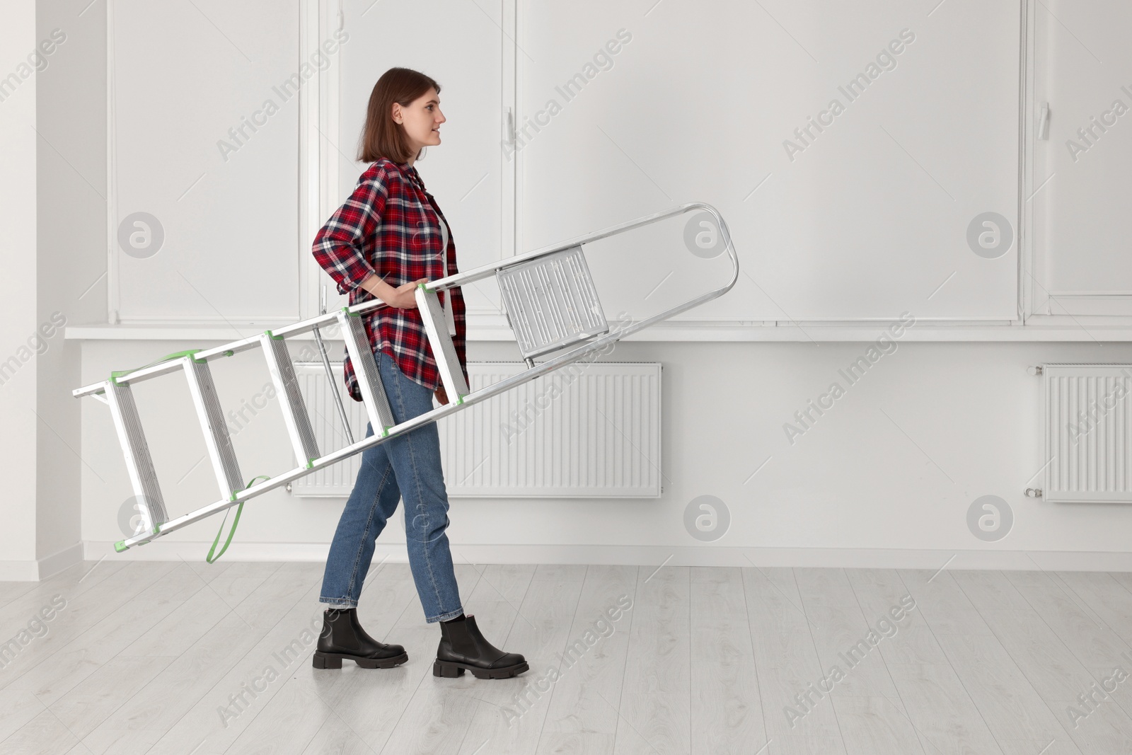 Photo of Young beautiful woman with metal stepladder indoors. Room renovation