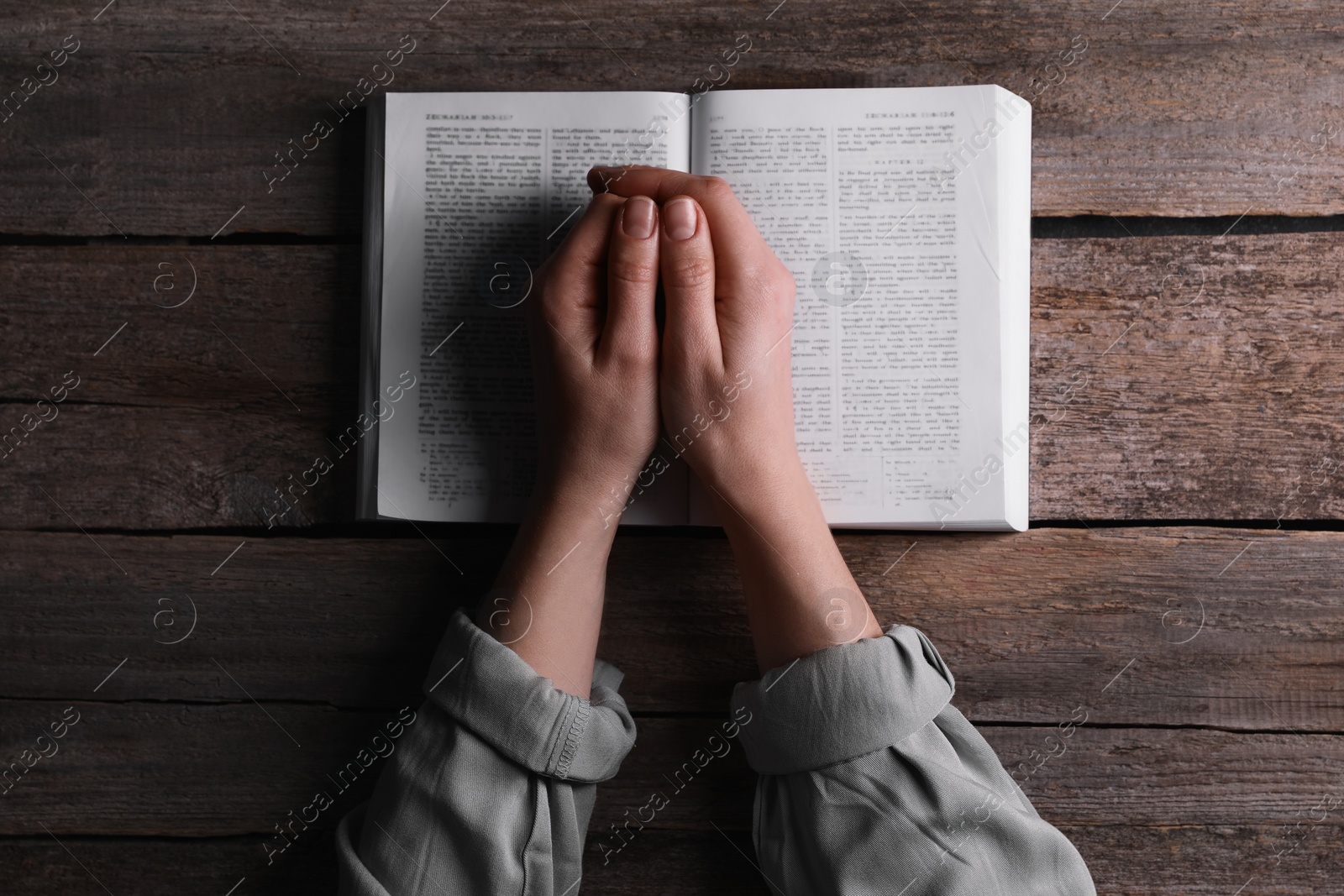 Photo of Religion. Christian woman praying over Bible at wooden table, top view