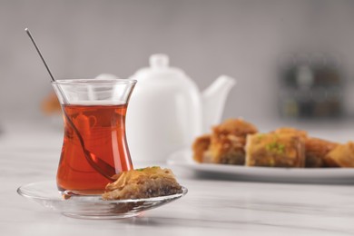 Glass of traditional Turkish tea and delicious baklava on white table, space for text