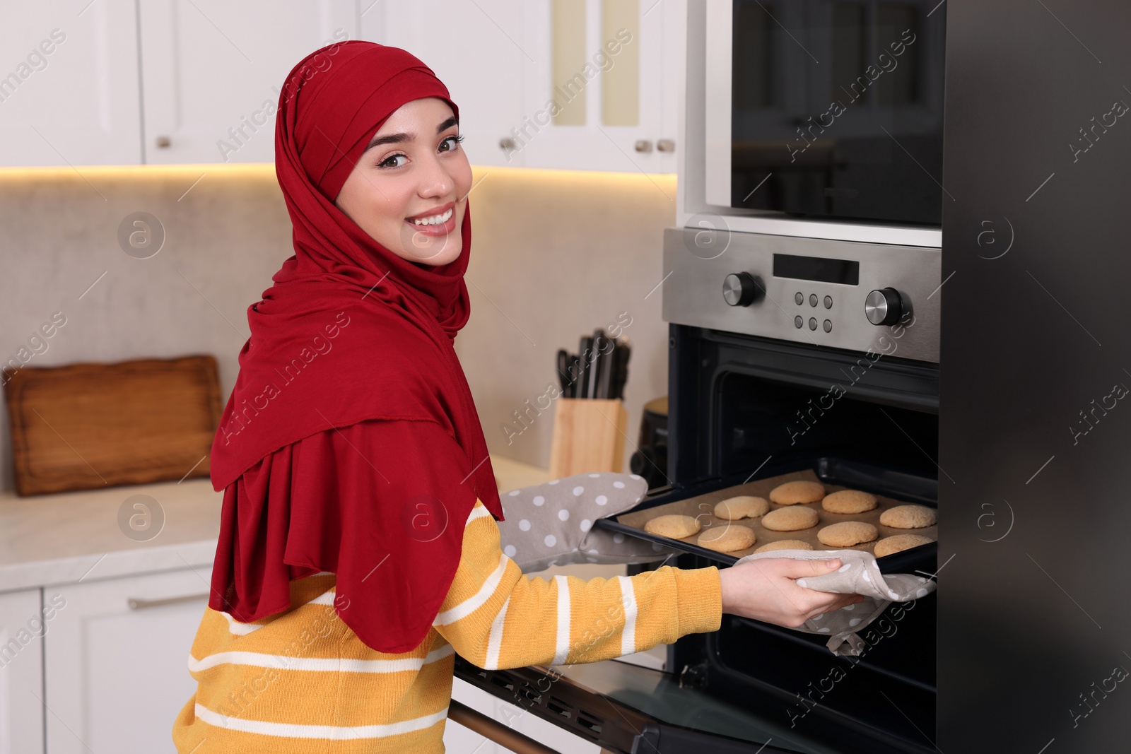 Photo of Muslim woman baking delicious cookies in oven at home