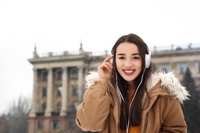 Photo of Beautiful young woman listening to music with headphones outdoors. Space for text