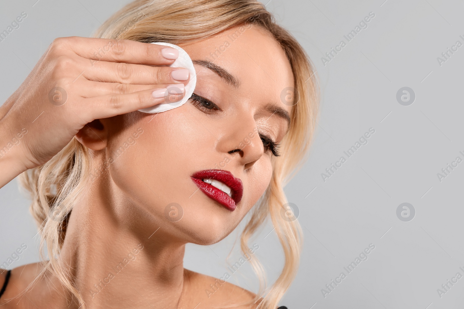 Photo of Beautiful woman removing makeup with cotton pad on light grey background, closeup. Space for text