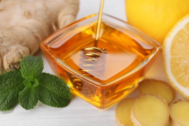 Photo of Natural cough remedies. Bowl with honey, ginger and mint on white table, closeup