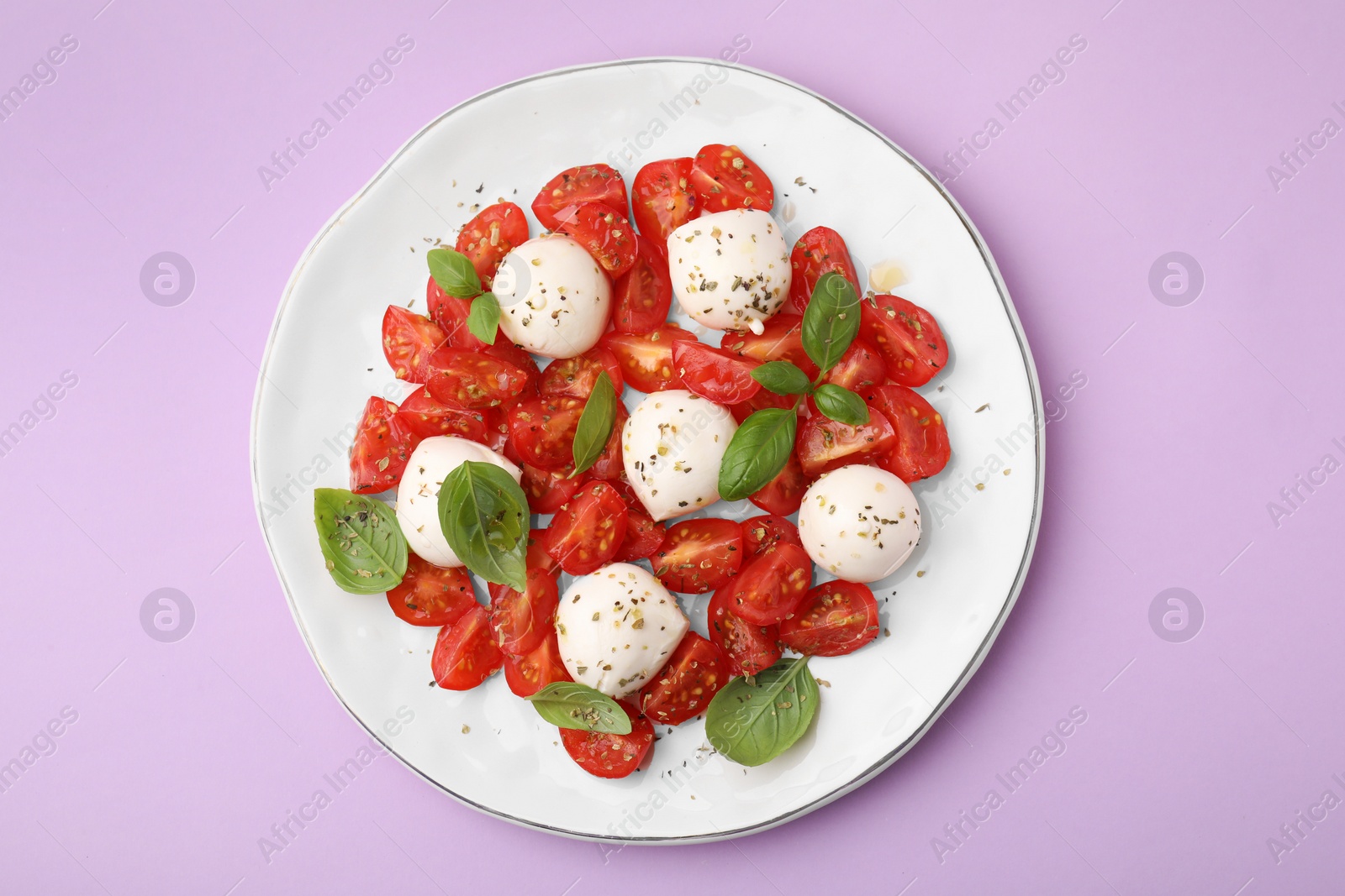 Photo of Tasty salad Caprese with tomatoes, mozzarella balls and basil on lilac background, top view