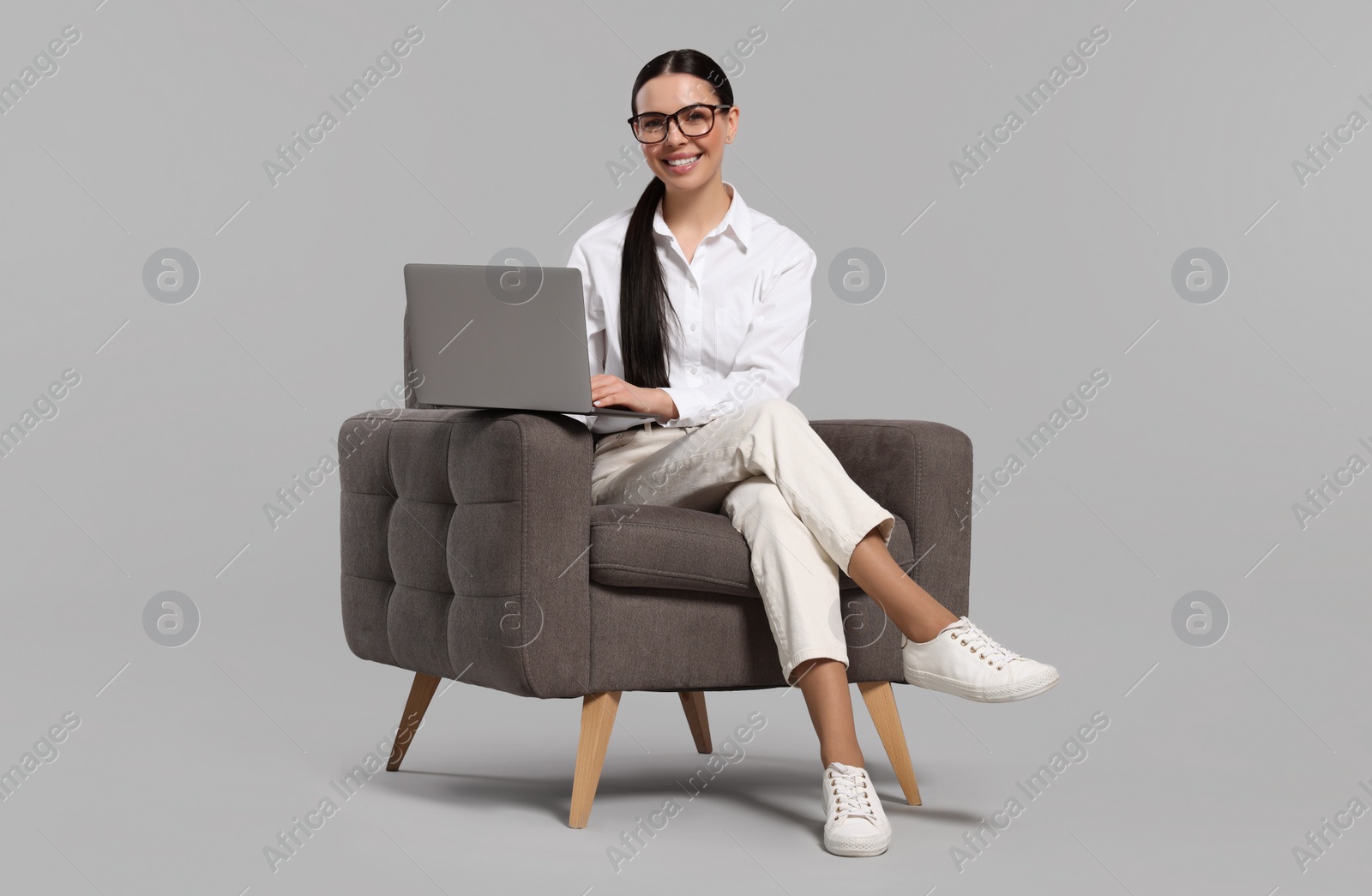 Photo of Happy woman with laptop sitting in armchair on light gray background