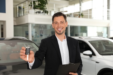 Photo of Salesman with clipboard and car key standing in salon