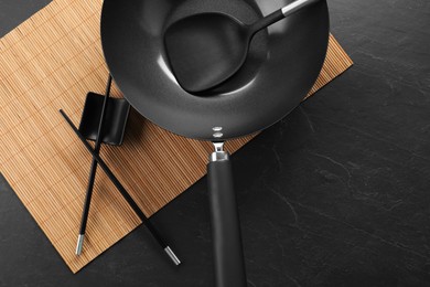 Photo of Black metal wok, chopsticks and spatula on dark textured table, top view
