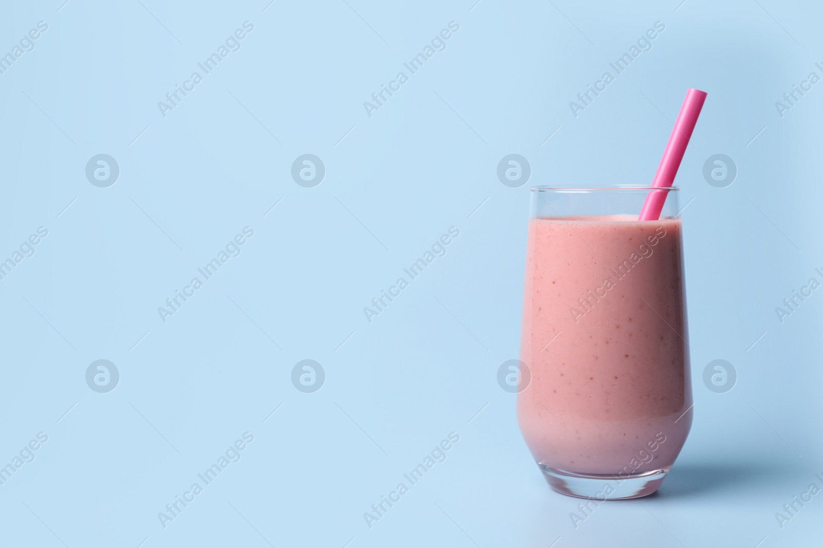 Photo of Glass with delicious berry smoothie and strawberries on light blue background. Space for text