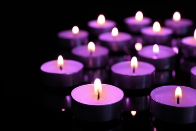 Image of Beautiful burning violet candles on black background. Funeral attributes