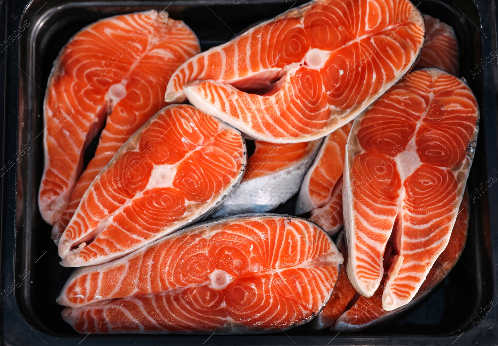 Photo of Steaks of fresh fish in container, top view