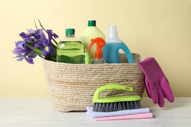 Spring cleaning. Wicker basket with detergents, flowers and gloves near tools on white wooden table