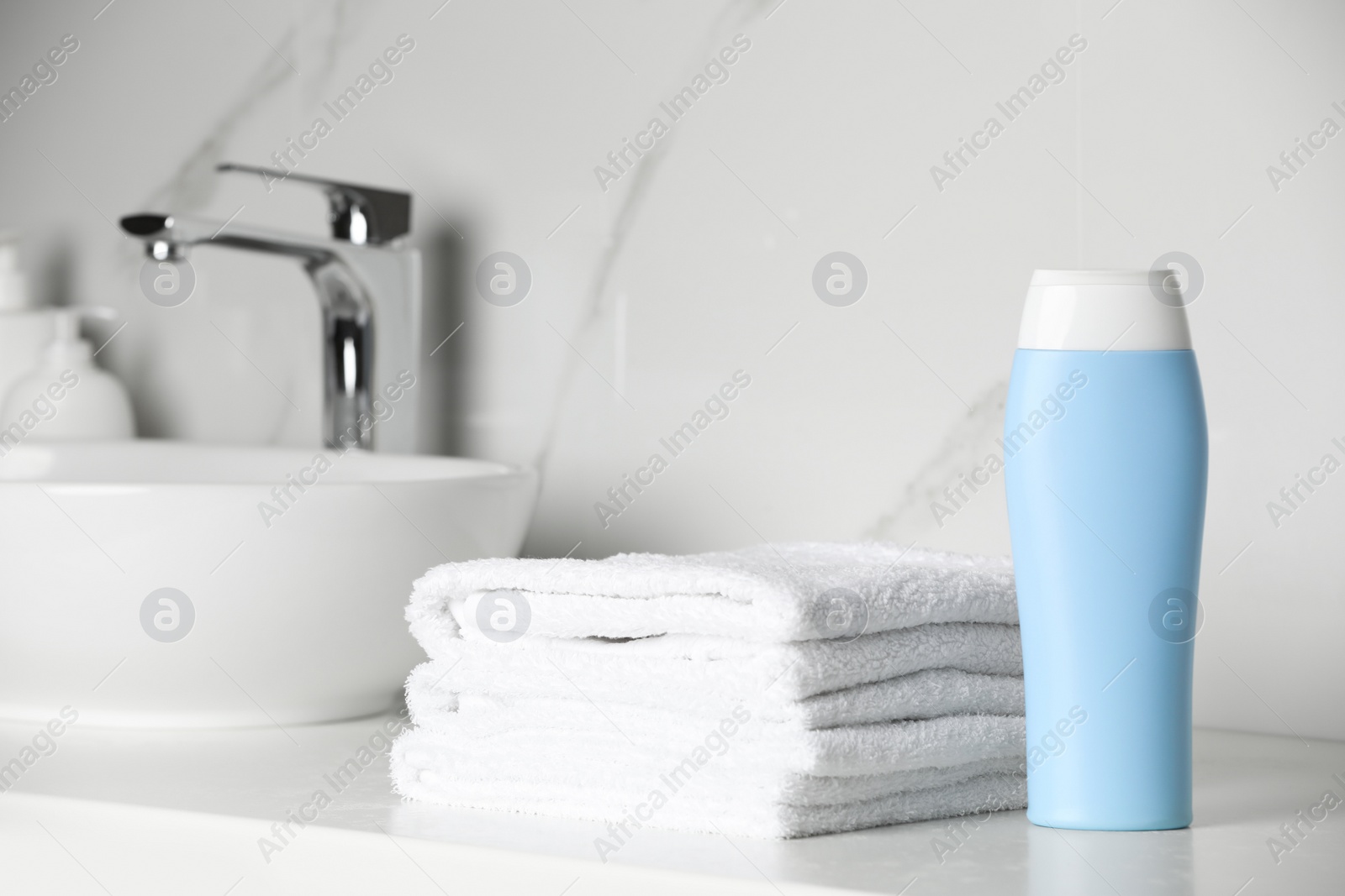 Photo of Bottle of shampoo and stacked towels near sink on bathroom counter, space for text