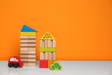Set of wooden toys on white table near orange wall, space for text. Children's development
