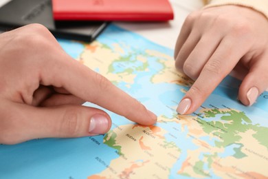Man and woman planning their honeymoon trip with world map at white wooden table, closeup