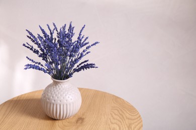 Photo of Bouquet of beautiful preserved lavender flowers on wooden table near beige wall, space for text