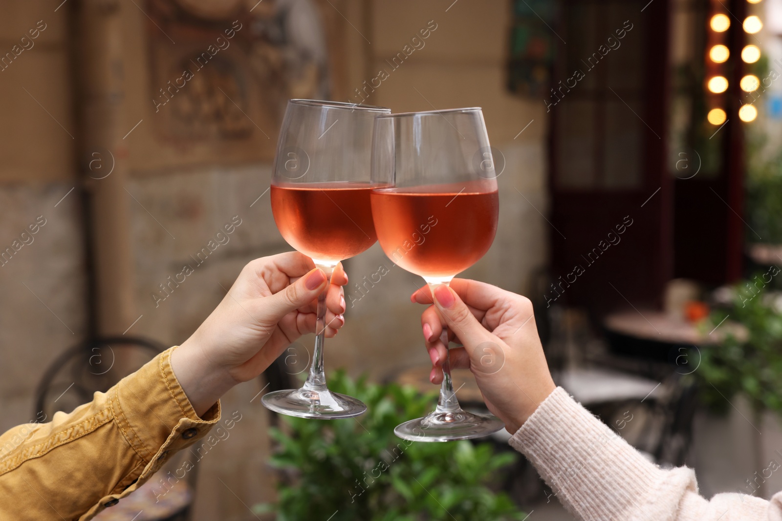 Photo of Women clinking glasses with rose wine outdoors, closeup