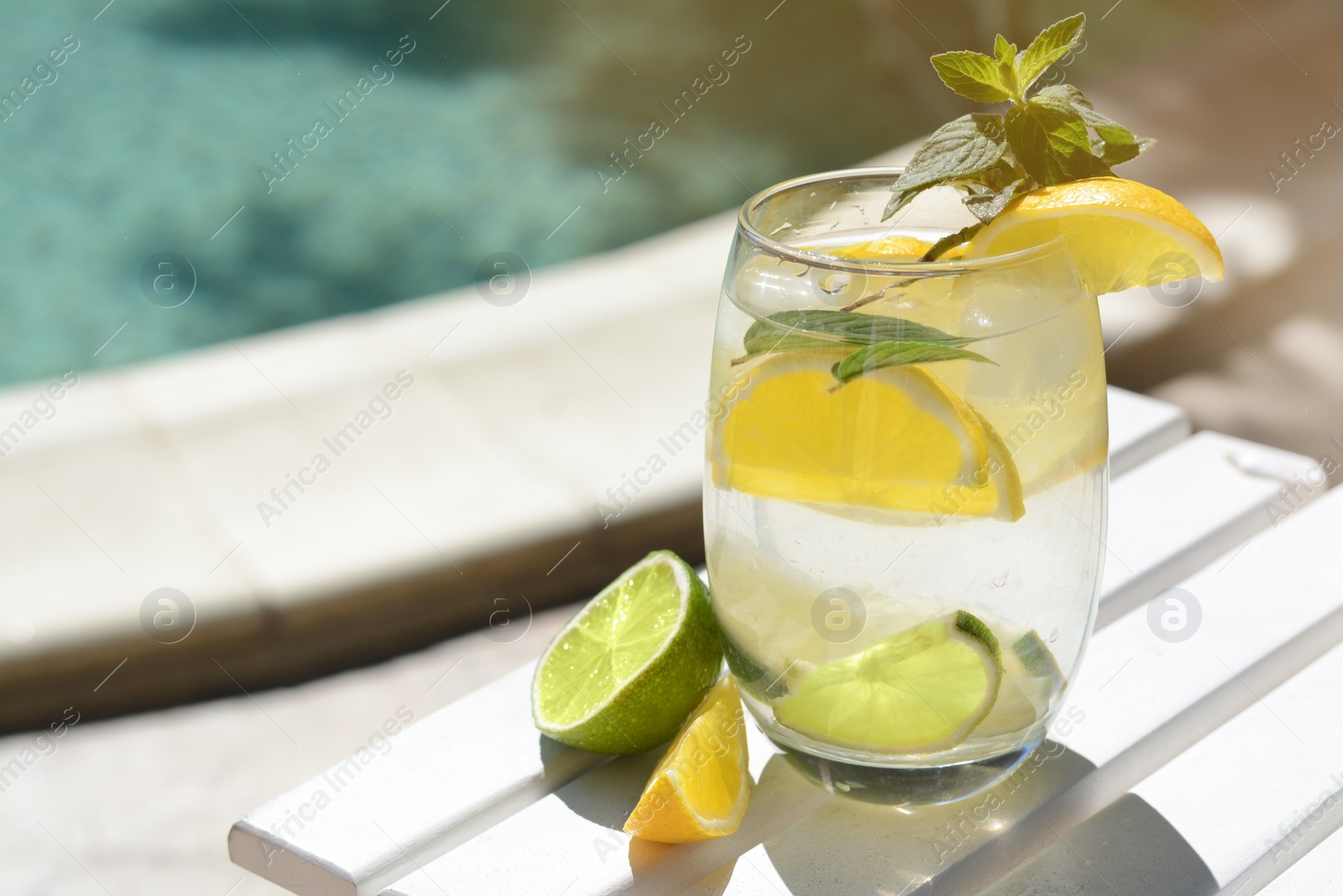 Photo of Refreshing drink with citrus slices and mint near swimming pool, closeup. Space for text