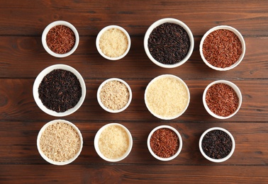 Photo of Bowls with different types of rice on wooden background, top view