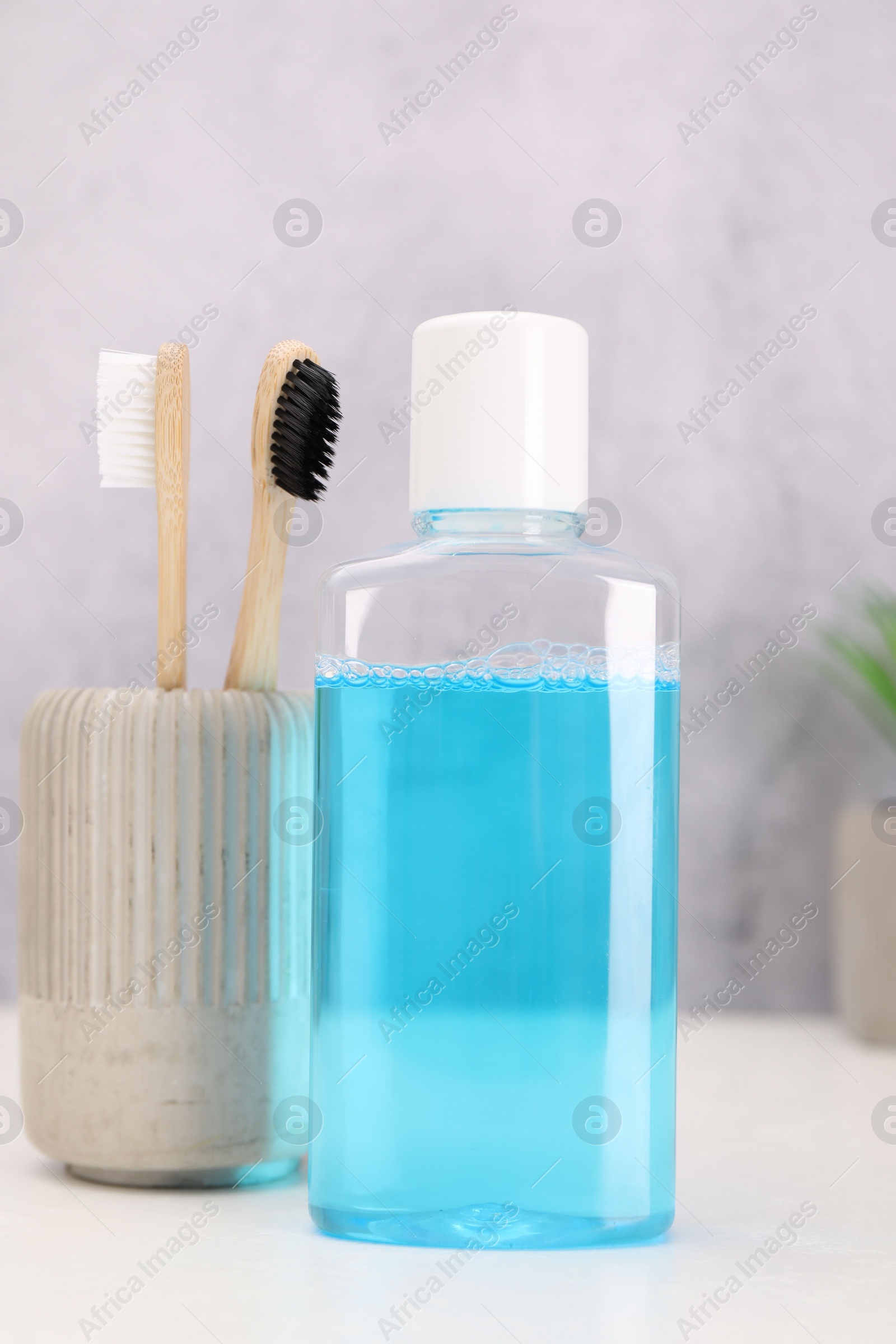 Photo of Bottle of mouthwash and toothbrushes on white table in bathroom