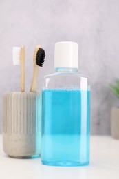 Bottle of mouthwash and toothbrushes on white table in bathroom