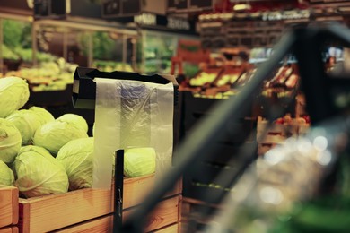 Plastic bags near rack with cabbages in supermarket