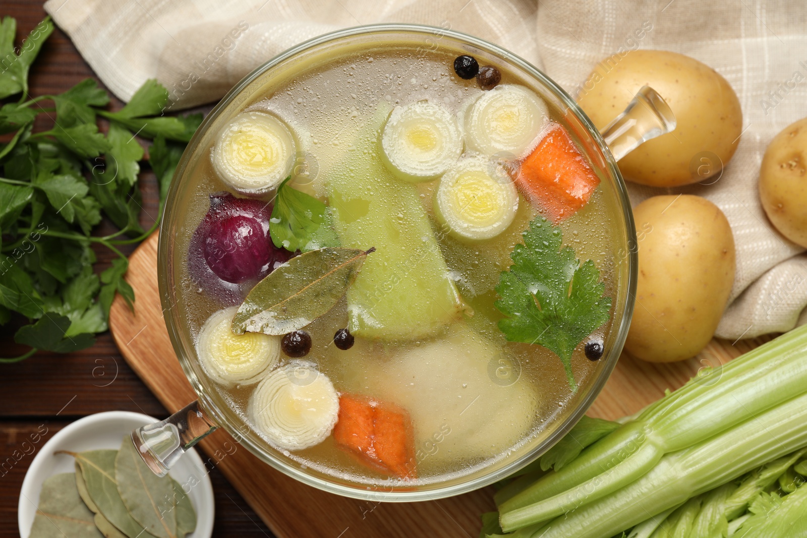 Photo of Glass pot with tasty bouillon and different ingredients on wooden table, flat lay