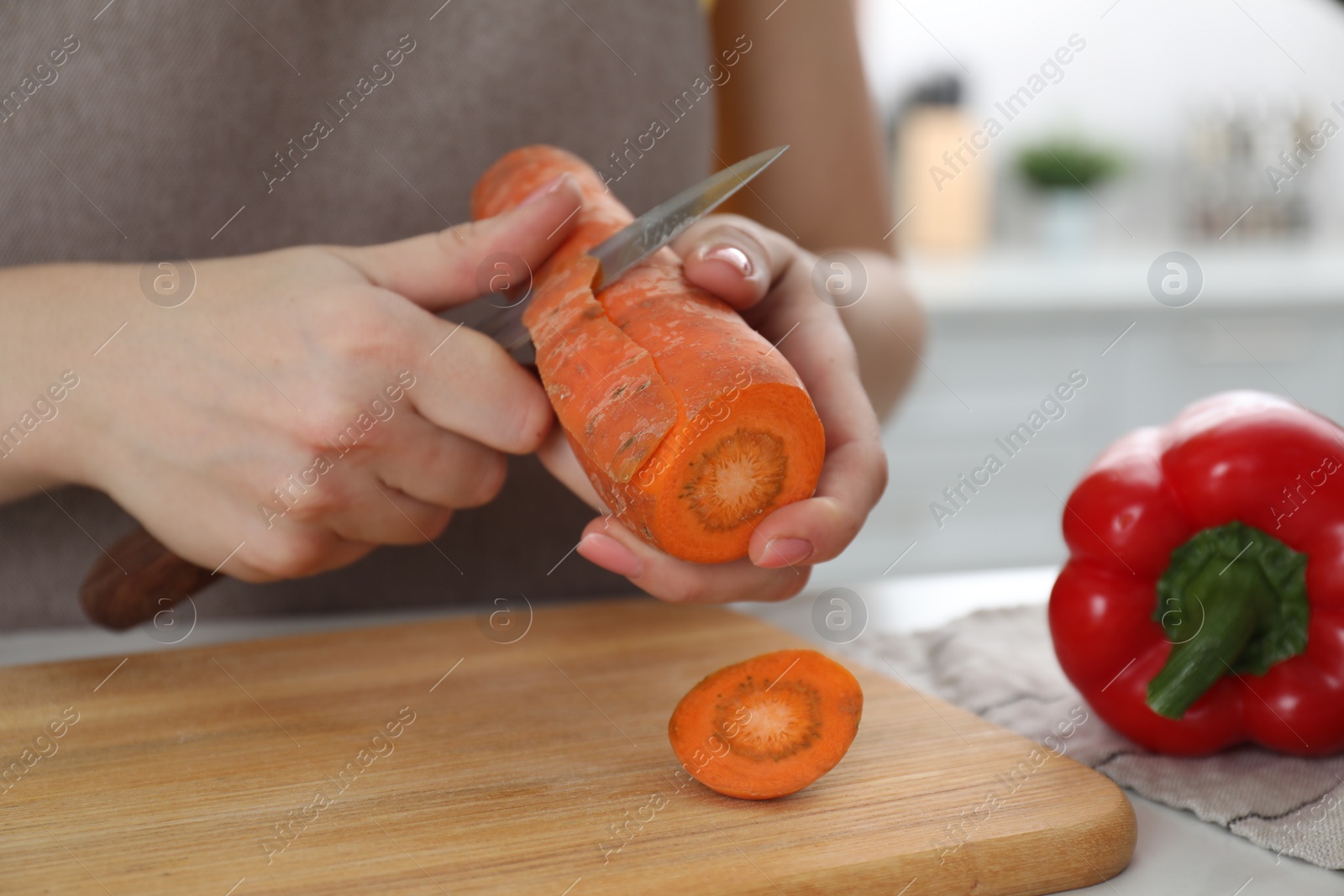 Photo of Woman peeling fresh carrot with knife at white marble table indoors, closeup