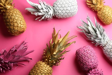 Different painted pineapples on pink background, above view. Creative concept