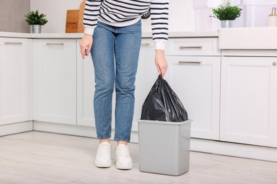 Photo of Woman taking garbage bag out of trash bin in kitchen, closeup