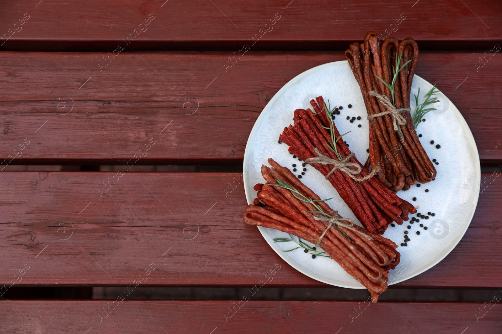 Photo of Tasty dry cured sausages (kabanosy) and spices on wooden table, top view. Space for text