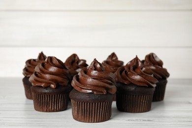 Photo of Delicious chocolate cupcakes with cream on white wooden table. Space for text