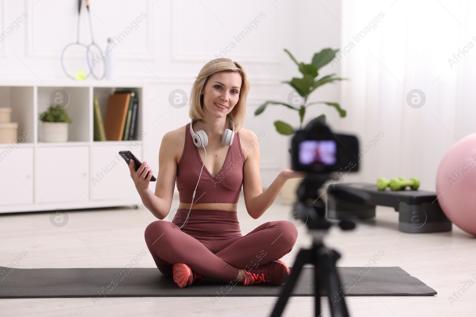 Photo of Smiling sports blogger recording fitness lesson with camera at home