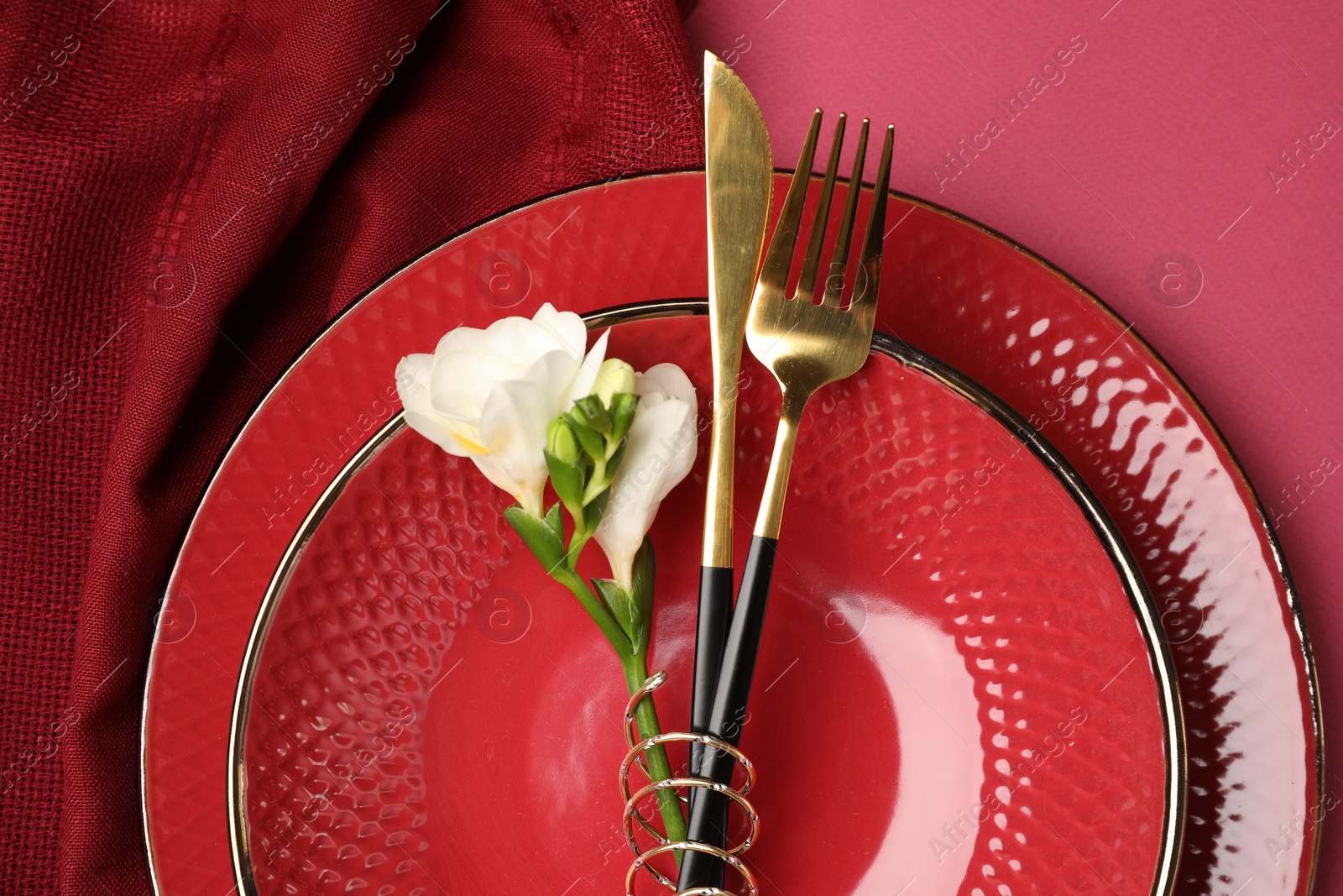 Photo of Stylish table setting with cutlery and floral decor on pink background, top view